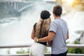 Happy tourist couple enjoying the view to Niagara Falls during romantic vacation. People looking to nature landscape at sunset tim