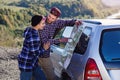 Happy tourist couple with paper map near car. Smiling young people using map. Traveling by rented car on summer Royalty Free Stock Photo