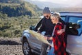 Happy tourist couple with paper map near rented car. Trendy young people using map. Traveling by car on summer vacations Royalty Free Stock Photo