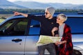 Happy tourist couple with paper map near rented car. Trendy young people using map. Traveling by car on summer vacations Royalty Free Stock Photo