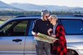 Happy tourist couple with paper map near rented car. Trendy young people using map. Traveling by car on summer vacations Royalty Free Stock Photo