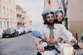 Happy tourist couple in protective hats are riding on rental vintage scooter in the Lisbon street Royalty Free Stock Photo