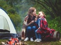 Happy tourist family on journey hike. mother and child fry sausages on bonfire near tent.