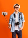 Happy tourist with selfie stick, camera and backpack over orange Royalty Free Stock Photo