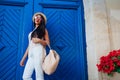 Happy tourist woman smiling against blue wooden door. Outdoor portrait of beautiful college girl wearing summer outfit Royalty Free Stock Photo