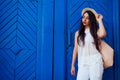 Happy tourist woman smiling against blue wooden door. Outdoor portrait of beautiful college girl wearing summer outfit Royalty Free Stock Photo