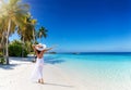 A happy tourist woman with white hat walks down a tropical paradise beach