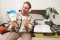 Happy tourist, young man shows passport and tickets, goes on holiday, sits with packed suitcase on bed, plans summer Royalty Free Stock Photo