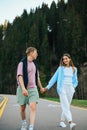 Happy tourists holding hands walk on a mountain road in the woods and smile looking at a loved one. Vertical Royalty Free Stock Photo