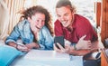 Happy travel bloggers watching instagram stories on smartphones, inside minivan - Digital nomads using mobile phones app -