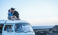 Happy travel couple kissing on minivan roof with ocean on back ground - Trendy people having fun during summer vacation - Love and