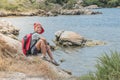 A happy traveler boy with backpack is sitting on rocks near the sea Royalty Free Stock Photo