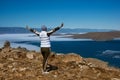 Happy traveler girl with raised hands standing on top of a mountain above lake in the spring holiday Royalty Free Stock Photo