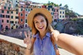 Happy traveler girl taking selfie photo doing victory sign on sunny day in Riomaggiore village, Cinque Terre, Italy Royalty Free Stock Photo