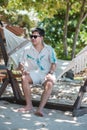 Happy traveler man with eyeglasses enjoy beautiful sea view, young man sitting on cradle at sand beach. Freedom, relaxing, Royalty Free Stock Photo