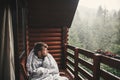 Happy traveler man resting in blanket on wooden porch with view on woods and mountains. Space for text. Hipster relaxing in Royalty Free Stock Photo