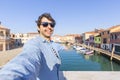 Happy traveler man taking a selfie on famous Murano island near Venice. Travel and vacation concept in Italy