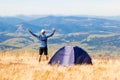 Happy traveler man on top of mountain raised hands enjoying freedom and view near tent camping outdoor. Travel adventure Royalty Free Stock Photo