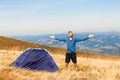 Happy traveler man on top of mountain raised hands enjoying freedom and view near tent camping outdoor. Travel adventure Royalty Free Stock Photo