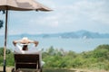 Happy traveler in white dress and hat enjoy beautiful sea view, young woman sitting on chair and looking ocean at tropical beach. Royalty Free Stock Photo