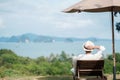 Happy traveler in white shirt and hat enjoy beautiful sea view, young man sitting on chair and looking ocean at tropical beach. Royalty Free Stock Photo