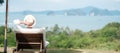 Happy traveler in white shirt and hat enjoy beautiful sea view, young man sitting on chair and looking ocean at tropical beach. Royalty Free Stock Photo