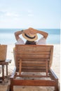 Happy traveler woman in white dress and hat enjoy beautiful sea view, young woman sitting on chair and looking ocean at tropical Royalty Free Stock Photo