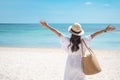 Happy traveler woman in white dress and hat enjoy beautiful sea view, young woman standing on sand and looking ocean at tropical