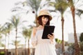 Happy traveling woman on white dress and straw hat using tablet reading news on the Internet Royalty Free Stock Photo