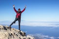 Happy traveller with camera and tripod standing on mountain peak with hands up