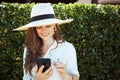 Happy trendy woman in shirt sending text message using phone