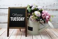 Happy Tuesday text on blackboard easel with flower bouquet on wooden background