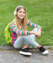 Happy tween girl with school backpack listening to music sitting on grass outdoors, education Royalty Free Stock Photo