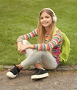 Happy tween girl with school backpack listening to music sitting on grass outdoors, education Royalty Free Stock Photo