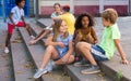 Happy tweenagers friends sitting on steps outdoors and chatting