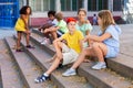 Happy tweenagers friends sitting on steps outdoors and chatting