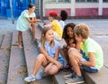 Happy tweenagers friends sitting on steps outdoors and chatting