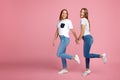 Happy two young twin sisters with beautiful smile walk over pink background. Royalty Free Stock Photo