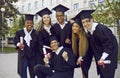 Happy university graduates in academic caps and gowns having fun on graduation day