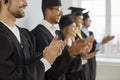 Happy university graduates in caps and gowns smiling and clapping hands at their graduation Royalty Free Stock Photo