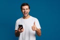 Happy unshaven guy showing thumb up while using mobile phone
