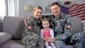 Happy US military family hugging on sofa smiling at camera nation and patriotism