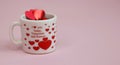 Happy Valentine`s Day greeting card.Holiday Valentine decoration.White glass cup with red glittering hearts on a pink background.