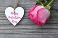 Happy Valentine`s Day greeting card with pink rose and decorative white heart with text on old wooden background.14th of February. Royalty Free Stock Photo