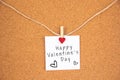 Happy Valentine`s day with heart sign on white paper pinned with red shining heart pegs on cork board