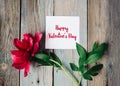 Happy Valentine`s day text on sheet of paper, red flower on old rustic wooden background Royalty Free Stock Photo