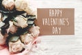 Happy Valentine`s Day text sign on craft greeting card and white roses bouquet on wooden background. Valentines day floral Royalty Free Stock Photo