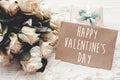 Happy Valentine`s Day text sign on craft greeting card and white roses, gift box on wooden background. Valentines day floral Royalty Free Stock Photo