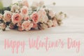 Happy Valentine`s Day text sign on pink small roses on wooden background in light. Tender Flowers image. Valentines day floral