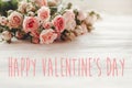 Happy Valentine`s Day text sign on pink small roses on wooden background in light. Tender Flowers image. Valentines day floral Royalty Free Stock Photo